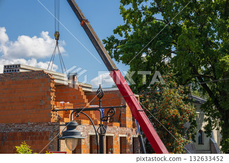A crane is lifting building materials to an unfinished house in a residential area on a sunny day 132633452