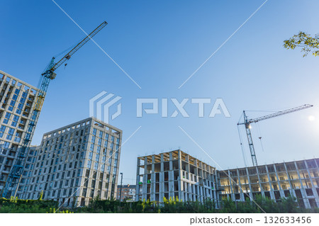 Builders are actively working on new residential structures at a construction site, with cranes and bright blue sky above 132633456