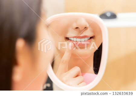 Woman checking her teeth with a hand mirror Woman checking her teeth with a hand mirror 132633639
