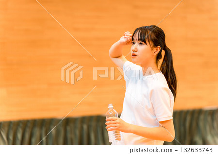小學、國中和高中的女生穿著運動服在體育館喝瓶裝水補充水分 132633743
