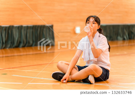 Elementary school, junior high school, and high school girls in tracksuits hydrating with bottled water in the gym Elementary school, junior high school, and high school girls in tracksuits hydrating with bottled water in the gym 132633746