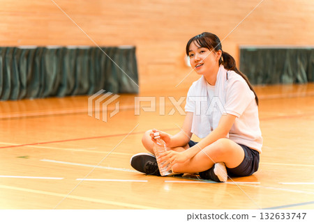 Elementary school, junior high school, and high school girls in tracksuits hydrating with bottled water in the gym Elementary school, junior high school, and high school girls in tracksuits hydrating with bottled water in the gym 132633747