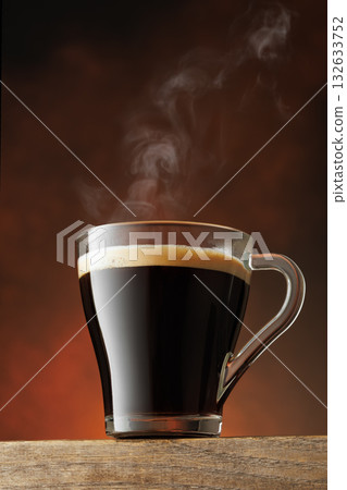 Steam rises from transparent cup of hot coffee standing on table against brown background Steam rises from transparent cup of hot coffee standing on table against brown background 132633752