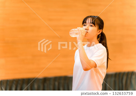 小學、國中和高中的女生穿著運動服在體育館喝瓶裝水補充水分 小學、國中和高中的女生穿著運動服在體育館喝瓶裝水補充水分 132633759