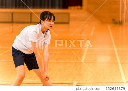 Junior high school and high school girls in gym clothes playing volleyball in a gym 132633879