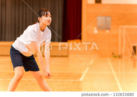 Junior high school and high school girls in gym clothes playing volleyball in a gym 132633880