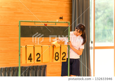 A female student in gym clothes flipping over a scoreboard in a gymnasium A female student in gym clothes flipping over a scoreboard in a gymnasium 132633946