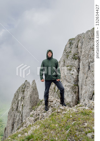 Man standing on rocky mountain ridge in foggy day with dramatic cliffs 132634427