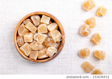 Candied ginger, crystallized ginger roots in a wooden bowl on linen. Rhizomes of Zingiber officinale, cut into block shaped chunks, boiled, and preserved with sugar. Sweet snack for the cold season. Candied ginger, crystallized ginger roots in a wooden bowl on linen. Rhizomes of Zingiber officinale, cut into block shaped chunks, boiled, and preserved with sugar. Sweet snack for the cold season. 132636412
