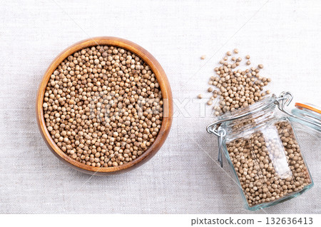 Whole and dried coriander seeds, in a wooden bowl on linen. Fruits of Coriandrum sativum, used as spice, with lemony citrus flavor, due to the terpenes linalool and pinene, that enhances when roasted. 132636413