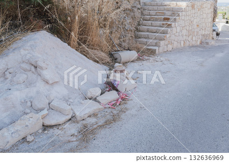 Abandoned construction waste and building materials (sand, stones, rubble) left on the roadside next to a renovated stone wall and stairs, illustrating neglect and cleanup costs Abandoned construction waste and building materials (sand, stones, rubble) left on the roadside next to a renovated stone wall and stairs, illustrating neglect and cleanup costs 132636969