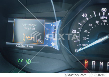 Close-up of a modern car dashboard, displaying an Oil Change Required warning light and message. Digital gauge cluster showing speedometer, fuel and battery status with high mileage 132636988