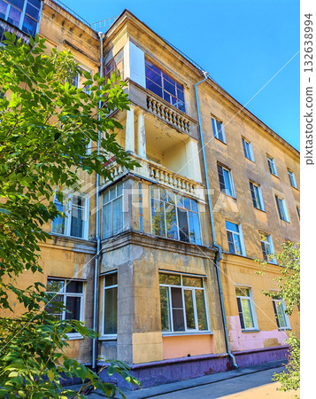 Old yellow residential building with worn balconies and decorative columns showing signs of plaster damage and weathering. The photo highlights facade aging and partial restoration, suitable for Old yellow residential building with worn balconies and decorative columns showing signs of plaster damage and weathering. The photo highlights facade aging and partial restoration, suitable for 132638994