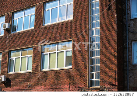 Lower part of an old red brick industrial building with damaged masonry, rusted metal door, and cracked plaster near the foundation. The photo emphasizes facade decay, material erosion, and neglected Lower part of an old red brick industrial building with damaged masonry, rusted metal door, and cracked plaster near the foundation. The photo emphasizes facade decay, material erosion, and neglected 132638997