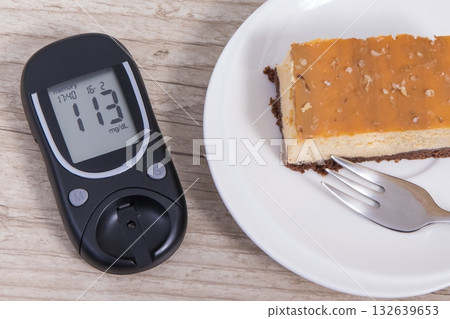Glucose meter with high result sugar level and portion of sweet cheesecake Glucose meter with high result sugar level and portion of sweet cheesecake 132639653