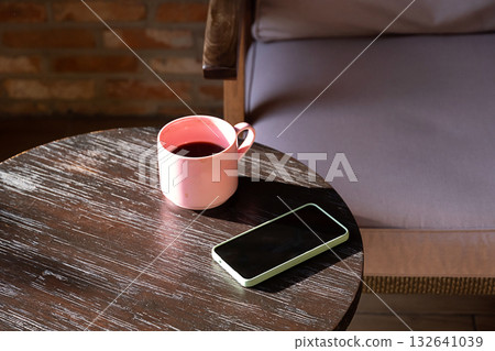 Pink coffee mug and phone on table in sunlight. 132641039