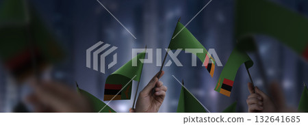 Zambia flags in their hands on a blurred urban background 132641685