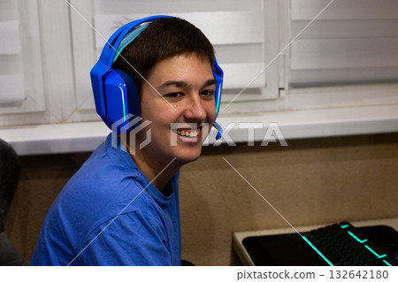 Truly authentic smile from video game player. Young man with headphones laughs heartily while relaxing with computer games, reflecting positive impact and vibrant emotions of online gaming 132642180