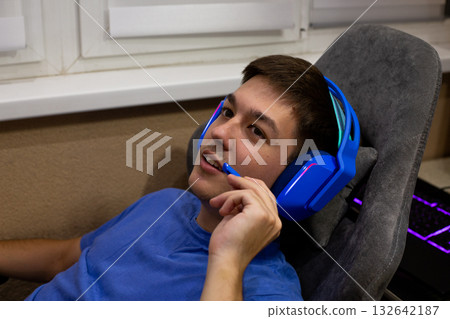 Guy leans back in his gaming chair and chats with his online friends on a headset. An alternative to live communication as an opportunity to develop lasting friendships Guy leans back in his gaming chair and chats with his online friends on a headset. An alternative to live communication as an opportunity to develop lasting friendships 132642187