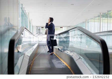 Businessman riding escalator Businessman riding escalator 132642232