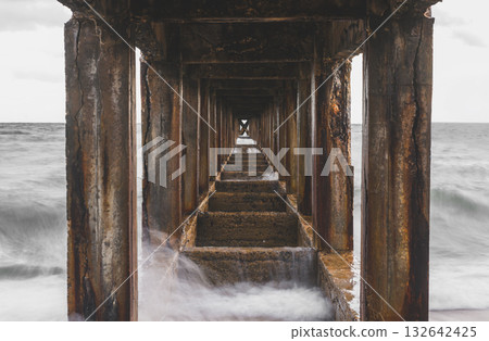 Symmetrical view under a pier with calm sea waves. Symmetrical view under a pier with calm sea waves. 132642425