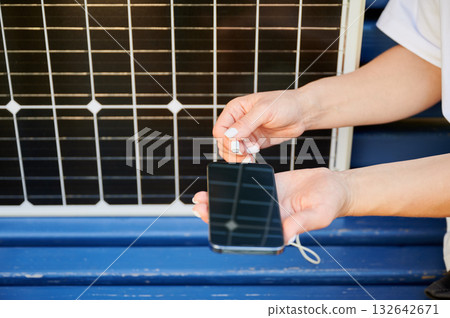 Close up view of woman charging her phone from solar battery. Young female using solar panel charger for mobile devices. Integration of sustainable renewable energy into everyday life. Close up view of woman charging her phone from solar battery. Young female using solar panel charger for mobile devices. Integration of sustainable renewable energy into everyday life. 132642671