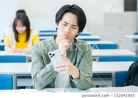 A university student worried while looking at his smartphone A university student worried while looking at his smartphone 132642883