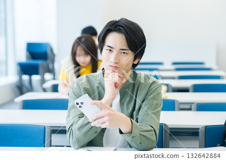 一名大學生憂心忡忡地看著他的智慧型手機 一名大學生憂心忡忡地看著他的智慧型手機 132642884