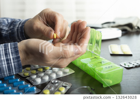 Middle aged caucasian man counts out pills for distributing scheduled dose of medication into pillbox Middle aged caucasian man counts out pills for distributing scheduled dose of medication into pillbox 132643028