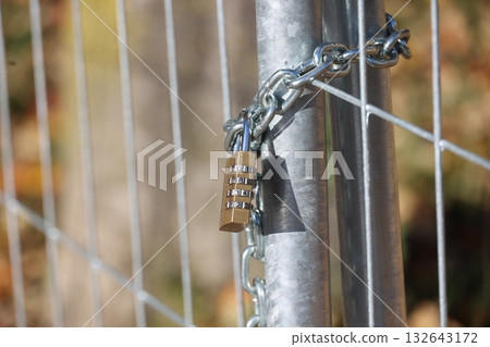 Chain is attached to a metal fence post with a lock on it Chain is attached to a metal fence post with a lock on it 132643172