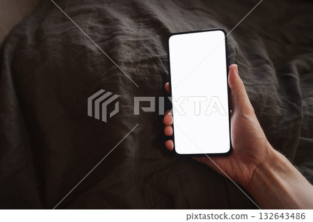 man hand holding phone with white screen over bed on background man hand holding phone with white screen over bed on background 132643486
