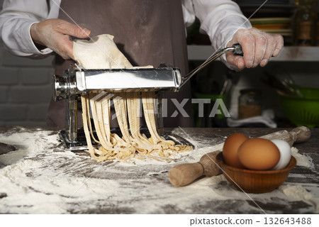 Caucasian female hands making fettuccine noodles using mechanical pasta machine Caucasian female hands making fettuccine noodles using mechanical pasta machine 132643488