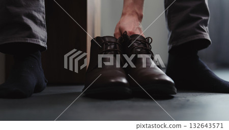 Young man put on his brown leather chukka boots indoor Young man put on his brown leather chukka boots indoor 132643571