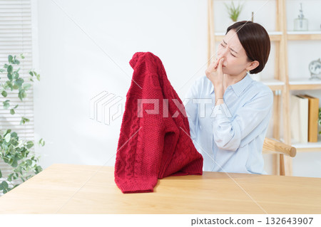 一位女士正在聞她拿出來準備換穿的毛衣。 132643907