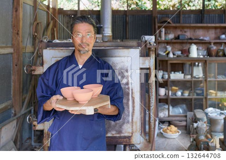 A potter in work clothes standing in front of a kiln A potter in work clothes standing in front of a kiln 132644708