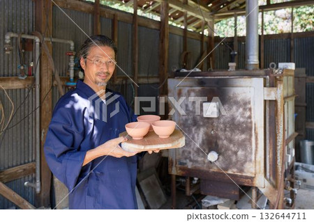 A veteran potter smiling in front of his kiln A veteran potter smiling in front of his kiln 132644711