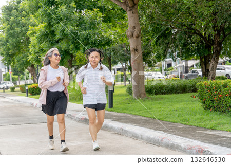 Two Asian senior women exercise with jogging along the road in the garden with day light. Two Asian senior women exercise with jogging along the road in the garden with day light. 132646530