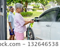 Asian senior woman use water nozzle to spray water for cleaning car in front of the house and support with senior man in the back. 132646538