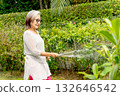 Asian senior woman use watering hose to water the plants in garden of her house. 132646542