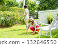 Asian senior woman use grass scissors to work in garden of her house with friend who stand and water the plants in the background. 132646550