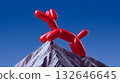 Balloon dog sculpture lifting a mountain peak against a blue sky 132646645