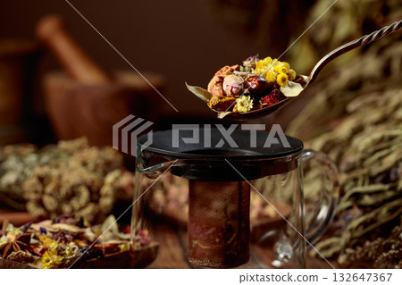 Various dried herbs and spices is poured into a glass teapot. Various dried herbs and spices is poured into a glass teapot. 132647367