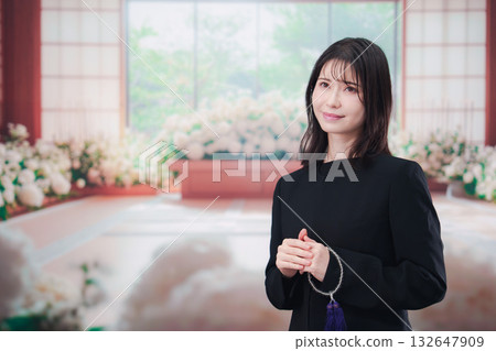 Young woman wearing mourning clothes and holding prayer beads at a funeral Young woman wearing mourning clothes and holding prayer beads at a funeral 132647909