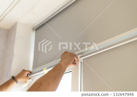 Male hands installing window blinds on modern window indoors. 132647948
