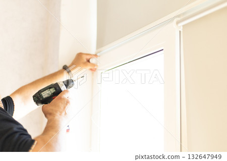 Professional handyman installing modern roller blinds on home windows. Professional handyman installing modern roller blinds on home windows. 132647949
