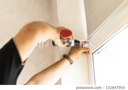 Man using screwdriver to attach roller blind mechanism to window during installation. Man using screwdriver to attach roller blind mechanism to window during installation. 132647950