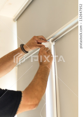 Installation of light gray roller blinds with reflective foil coating on windows. Installation of light gray roller blinds with reflective foil coating on windows. 132647952