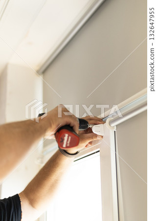 Worker using screwdriver to fasten roller blind components on window frame. Worker using screwdriver to fasten roller blind components on window frame. 132647955