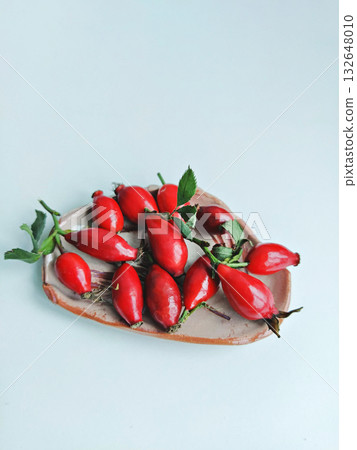 Fresh rose hips on heart wooden board with green leaves, minimal composition and bright natural color Fresh rose hips on heart wooden board with green leaves, minimal composition and bright natural color 132648010