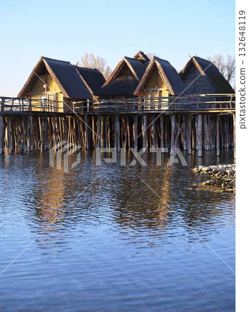Elegant wooden houses on stilts reflecting in calm water at sunset in a serene lakeside location 132648119